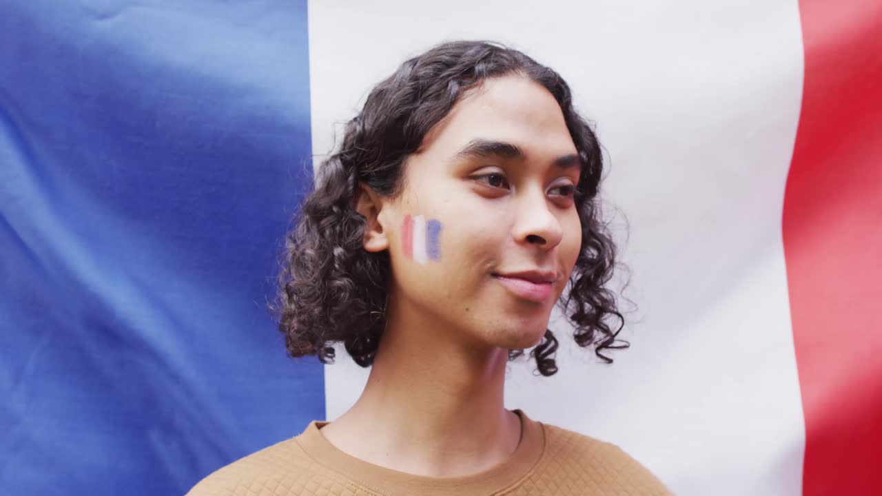 retrato de un hombre biracial feliz con la bandera de francia en el fondo y en la mejilla