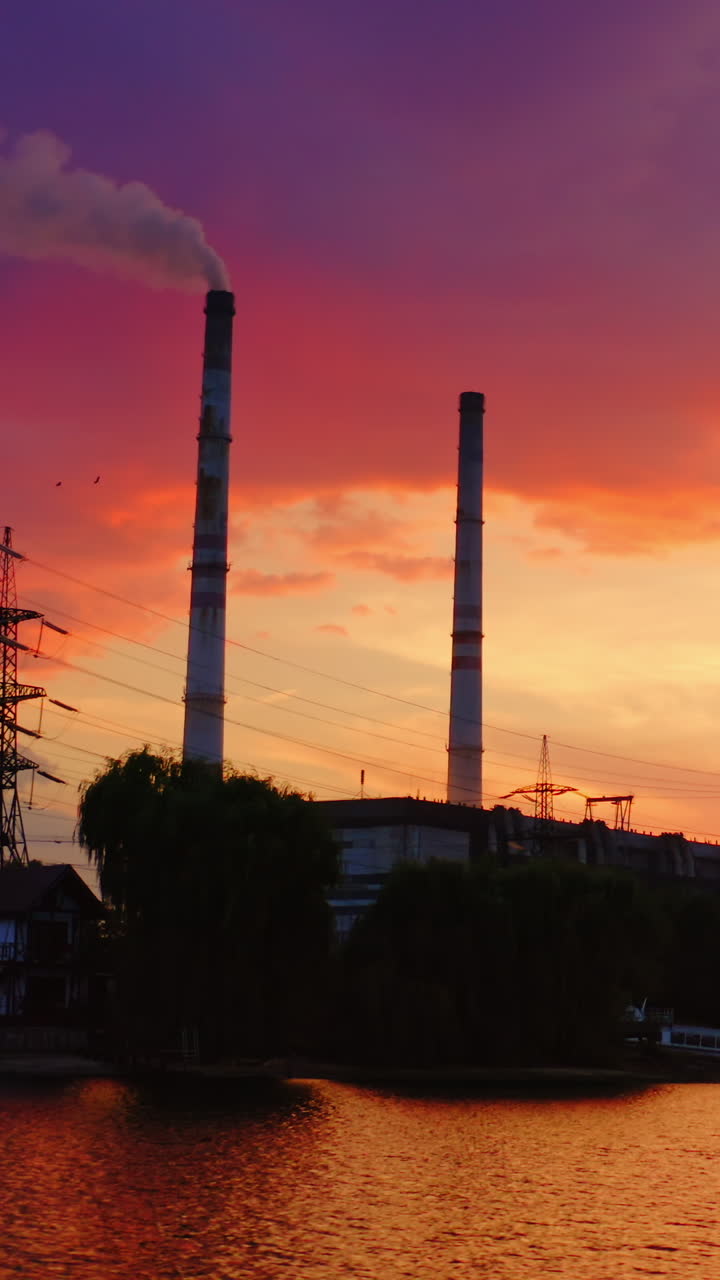 Industry against beautiful evening sky. Chemical factory and high-voltage electric lines on the riverbank at sunset. Pollution of the environment. Vertical video