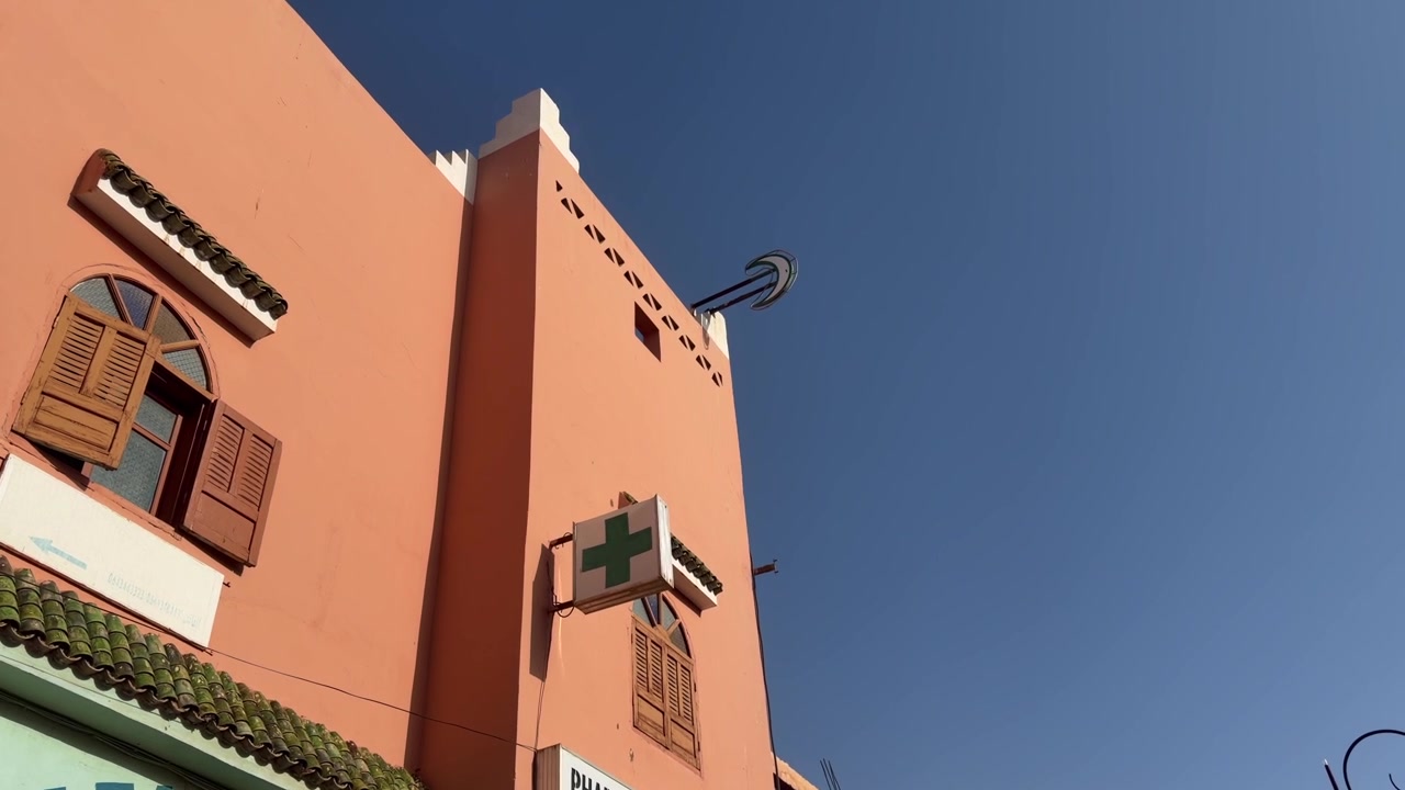 Insegna a croce verde di farmacia montata su un edificio marocchino rosa con dettagli architettonici tradizionali