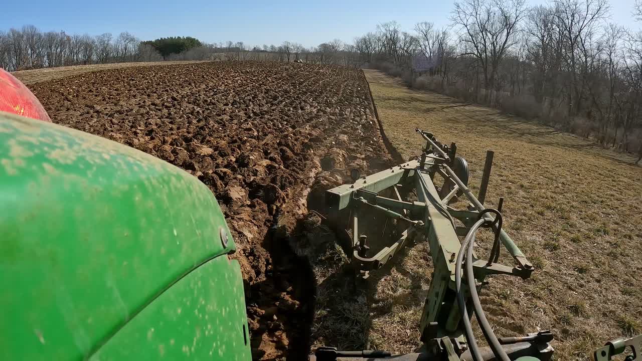 POV - Farmer on green agricultural tractor prepares field for planting and raises plows at end of row