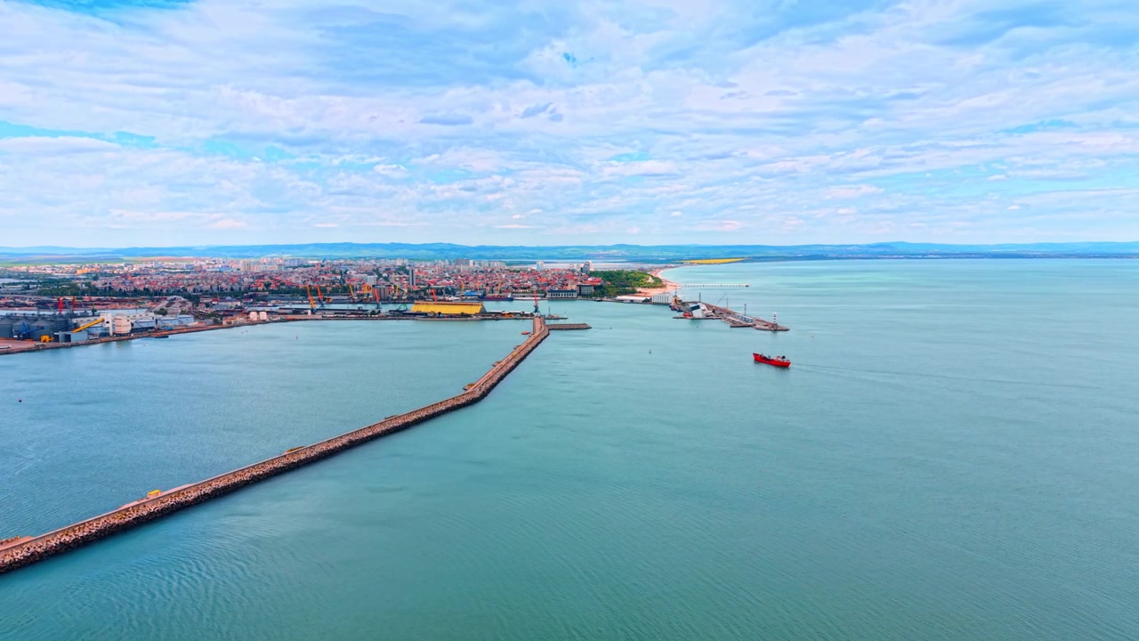 Vista aerea dall'alto di una lunga diga foranea in un porto industriale. Ampia ripresa aerea di una lunga diga foranea in cemento che protegge un porto commerciale industriale con una nave rossa