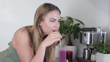 slow motion medium shot of a beautiful blonde young women stirring purple blueberry smoothie then taking a drink after and getting a brain freeze