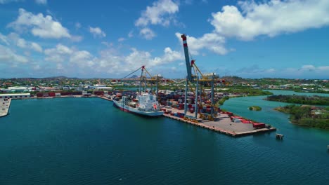 shipping container port with a small boat docked and 2 cranes, cinematic aerial drone tilt down