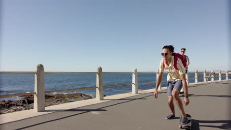 happy diverse gay male couple using scooter and skateboard at promenade by the sea, slow motion