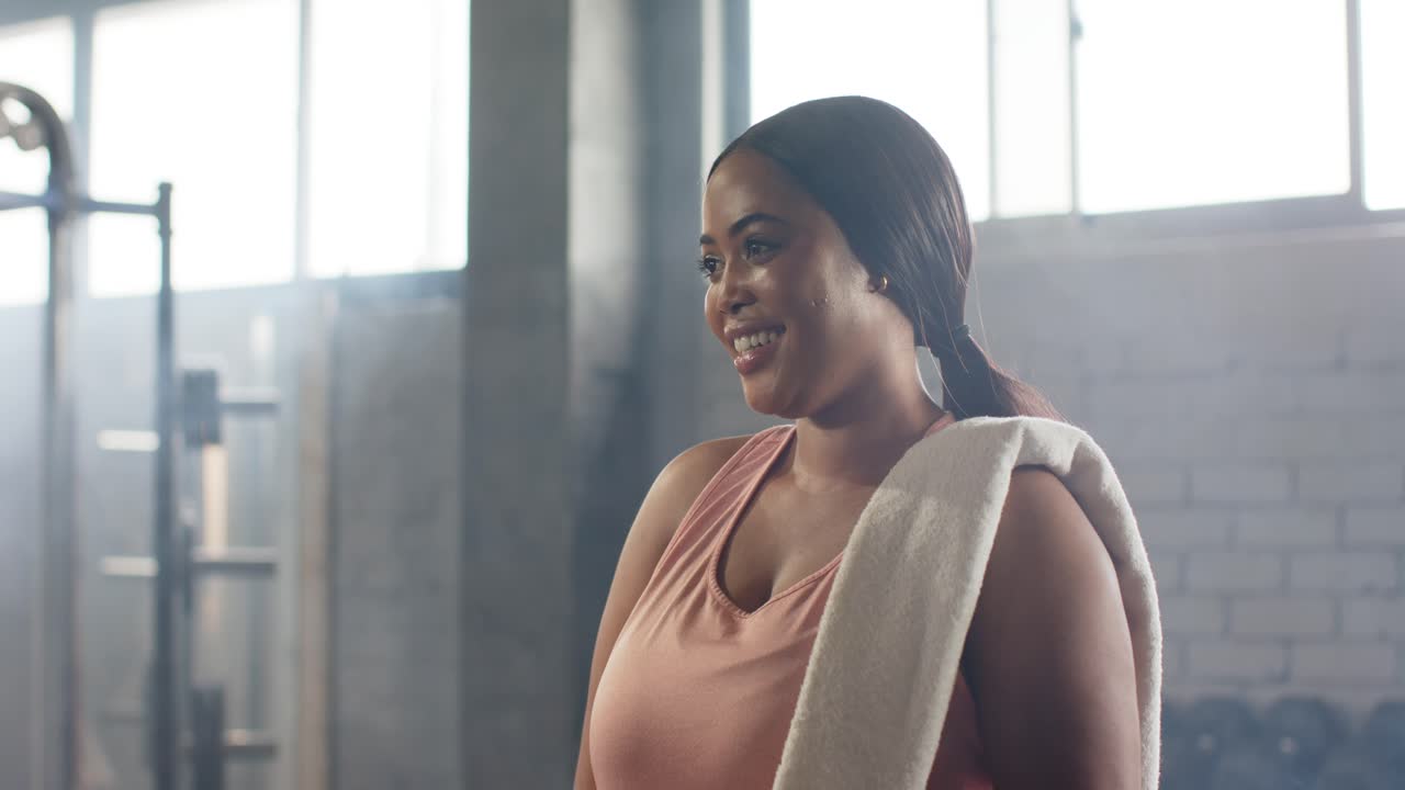 Camera panning up African American woman adjusting towel, lifting shaker during cool-down in gym