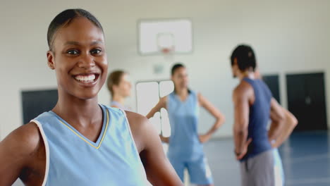 smiling female basketball player in uniform standing in gym with teammates, copy space