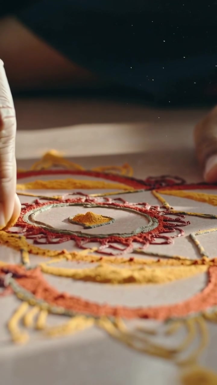 Video verticale: Mani artigiane sospese che pizzicano e lasciano cadere polvere colorata su una tavola, formando un mandala