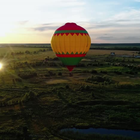 beautiful aerostat against the evening sunlight. colorful round hot air balloon flying over the green nature. airship in the air in rural place at sunset. aerial view.