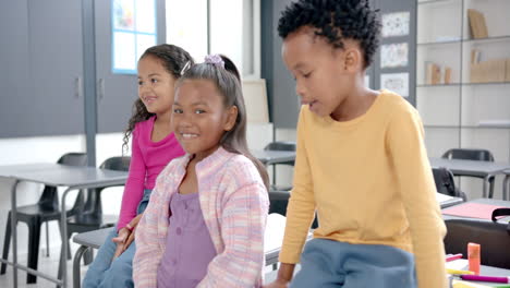 in school, two biracial girls and one african american boy are sitting in a classroom