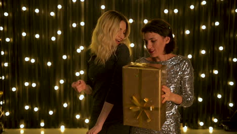 young beautiful women dancing with a golden gift box and wearing evening dresses