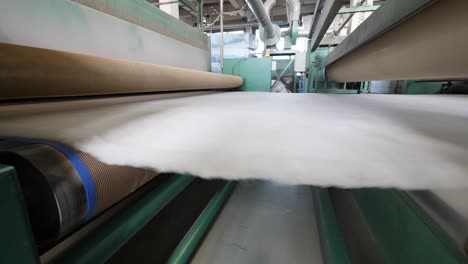 metal rollers move white polyester fabric while working at a plant.