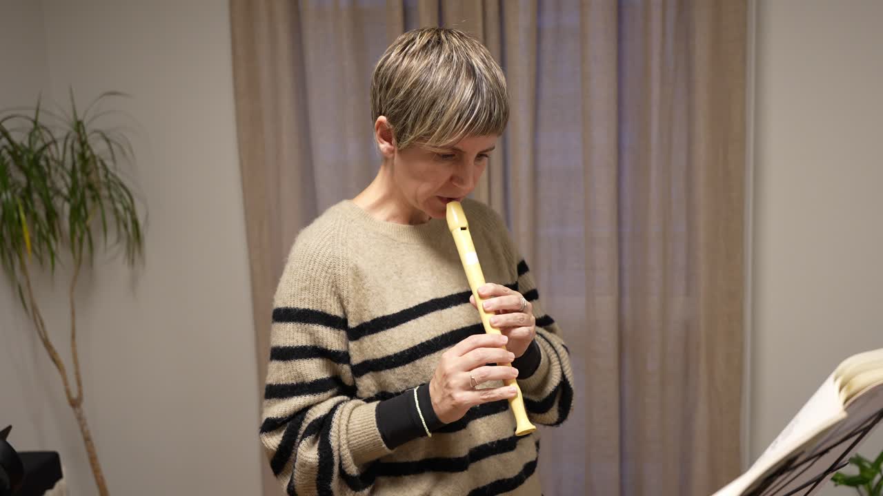 Donna che suona un flauto dolce mentre legge uno spartito musicale al chiuso