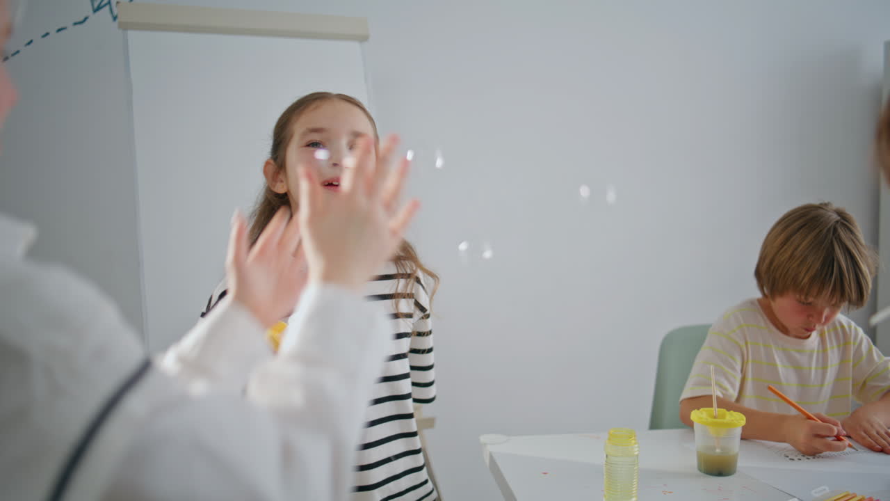 Kid girl playing soap bubbles in school break closeup. Classmates free time