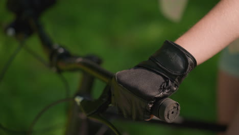 close-up of individual gripping bike handlebar with gloved hand, throttle and brake in use, sunlight gently reflects off gloved hand, with a softly blurred green background