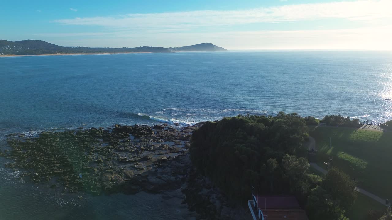Drone aerial landscape of ocean sea waves breaking along rocky headland reef coastline from Terrigal The Haven with bushland forest and cliffs on horizon Central Coast Australia travel tourism nature