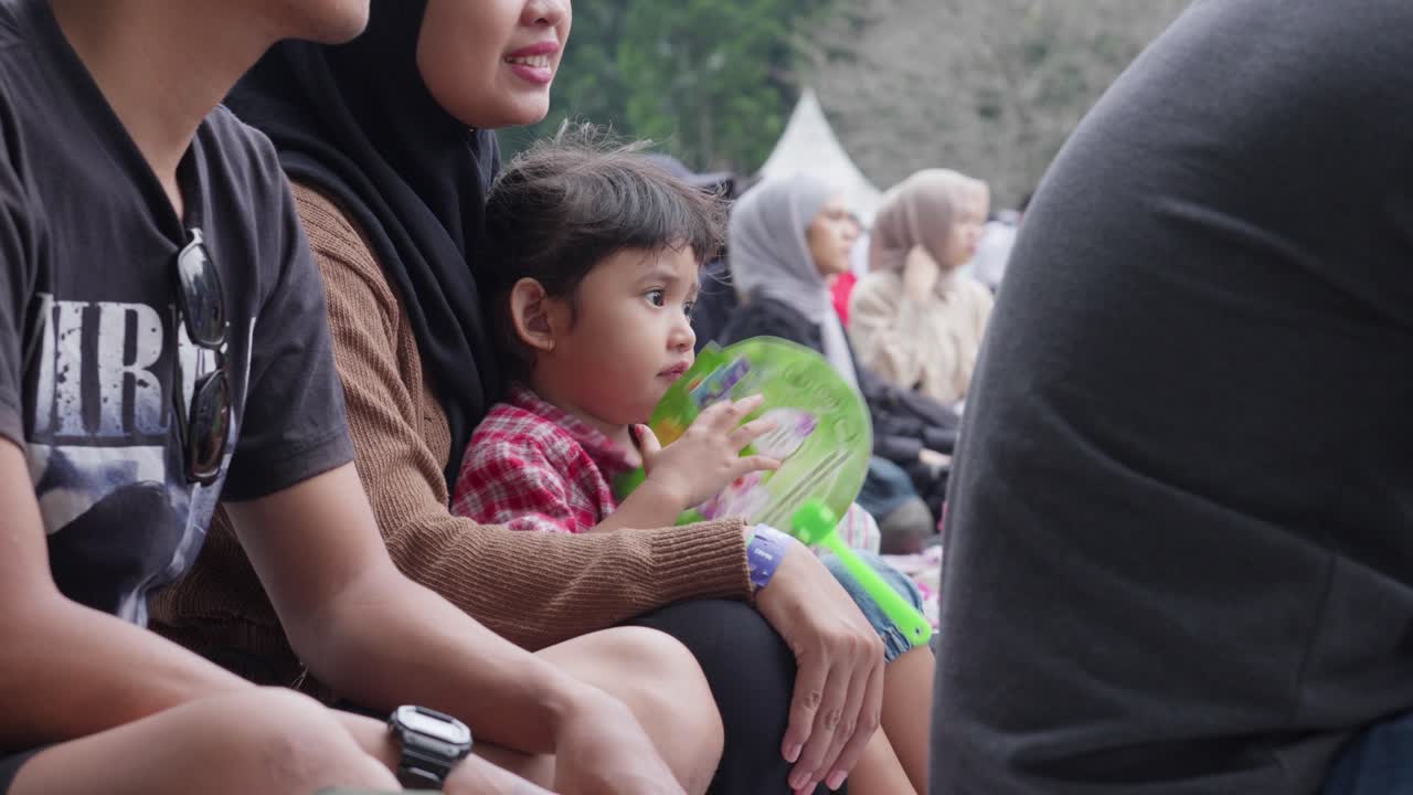 Young child enjoying an outdoor concert with family at Kebun Raya Bogor