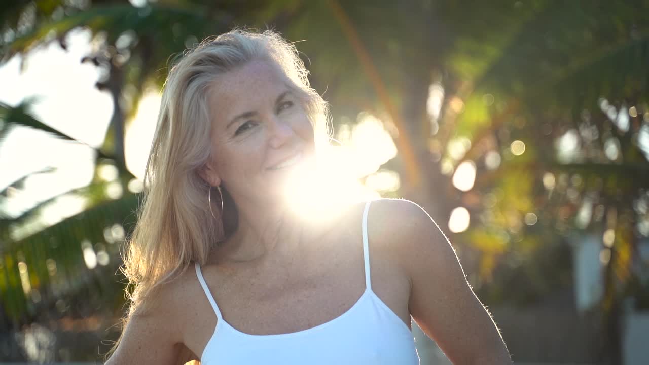 Mulher loira madura e sexy em câmera lenta com luz de fundo balançando a cabeça e sorrindo para a câmera