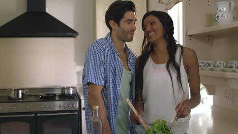 hombre besando a una mujer mientras mezcla una ensalada en la cocina