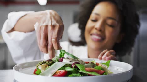 African-american-female-chef-garnishing-dish-and-similing-in-restaurant-kitchen