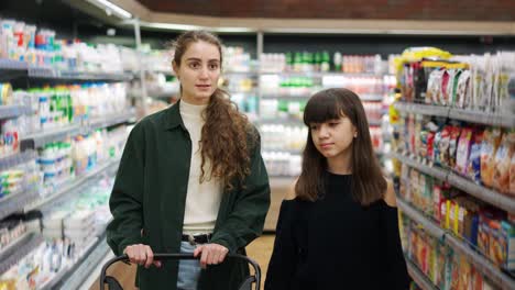 Teen-girl-and-her-mom-or-sister-shopping-in-the-supermarket-with-cart