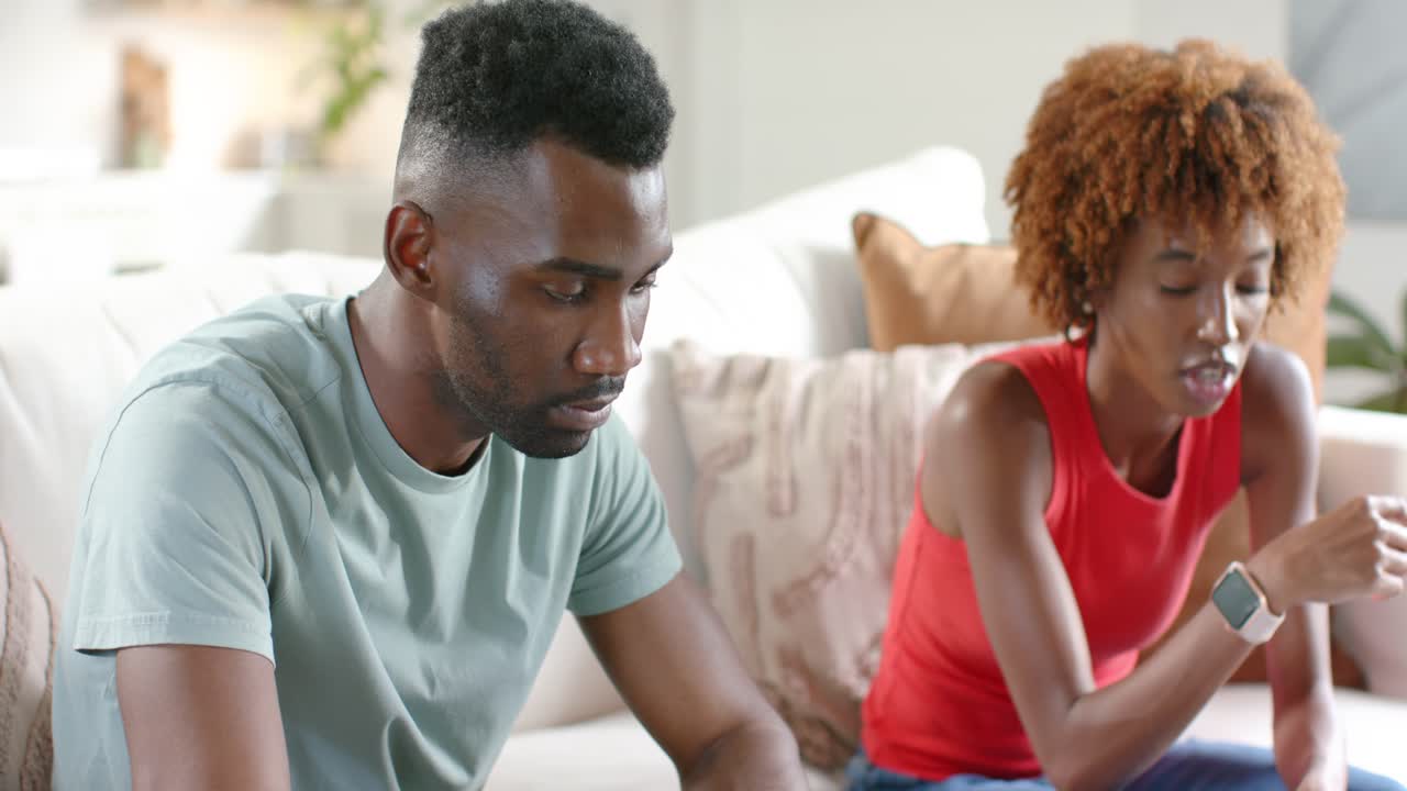 Diverse couple working on laptop in lounge while woman gesturing and speaking, causing man glancing