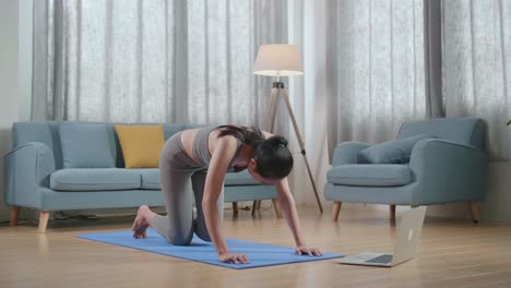 joven atleta asiática haciendo ejercicio, estirándose y practicando yoga en casa con un entrenador en línea a través de una computadora portátil