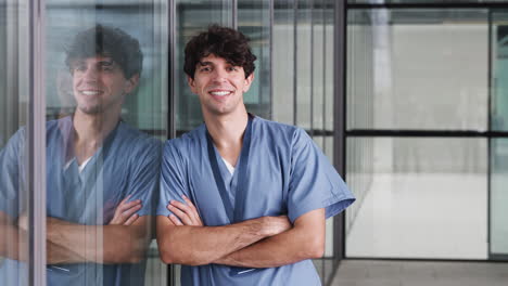 Portrait-Of-Male-Doctor-Wearing-Scrubs-Standing-In-Modern-Hospital-Building