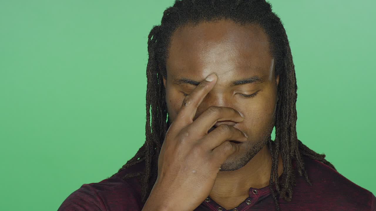 un hombre negro con dreads mirando triste y cubriendo su cara con sus manos, en un fondo de estudio de pantalla verde