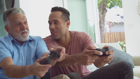 hispanic father with adult son sitting on sofa at home playing video game together