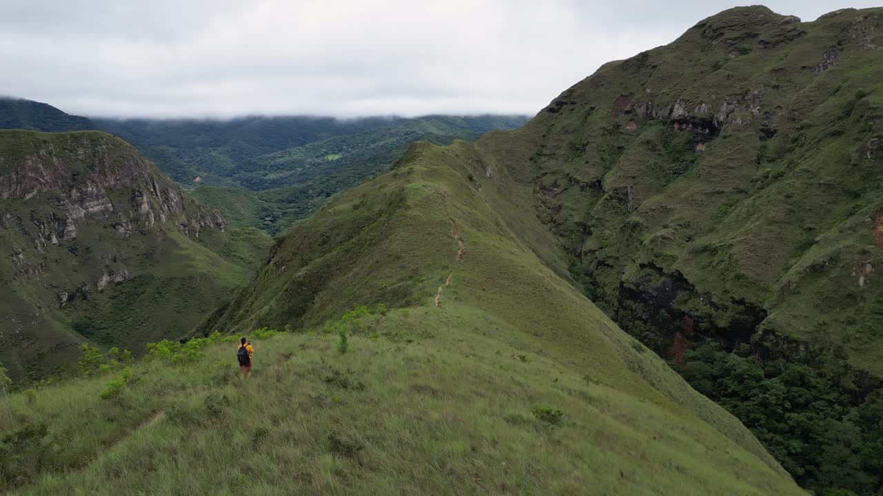 Flyover hiking trail to hiker taking picture on grassy mountain ridge