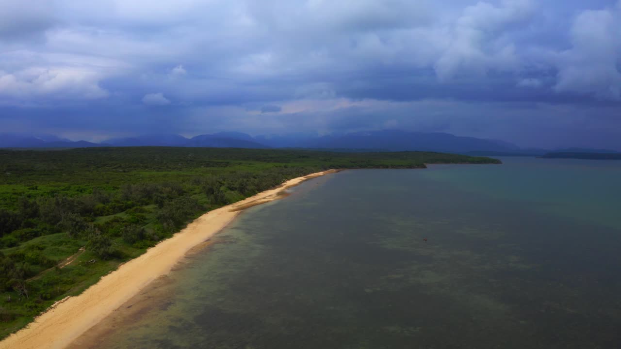 desde arriba, el dron captura una vista impresionante de la playa tropical a medida que emerge de las nubes, su belleza y tranquilidad no se ven atenuadas por el cielo gris sobre su cabeza.