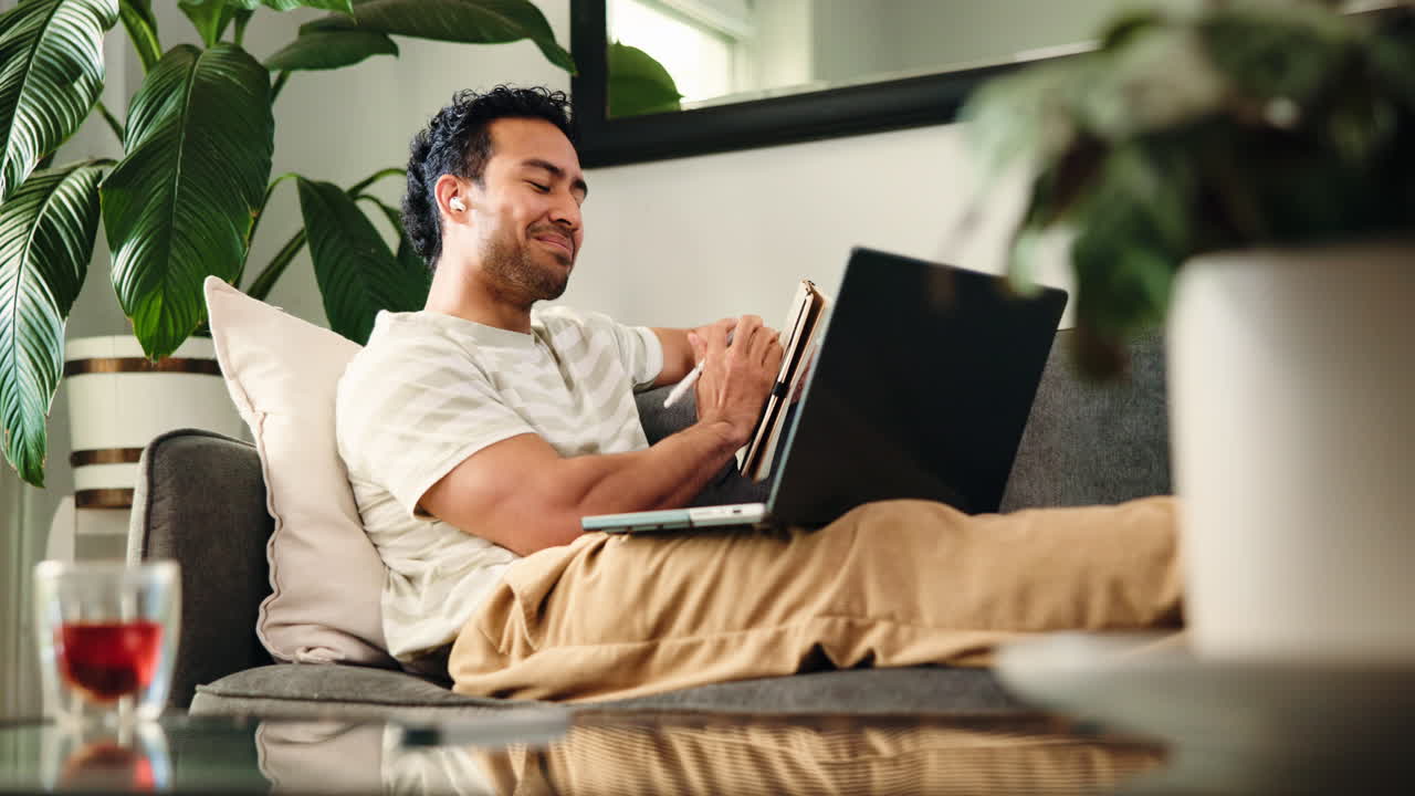 Focused Man Taking Notes While Using Laptop on Couch