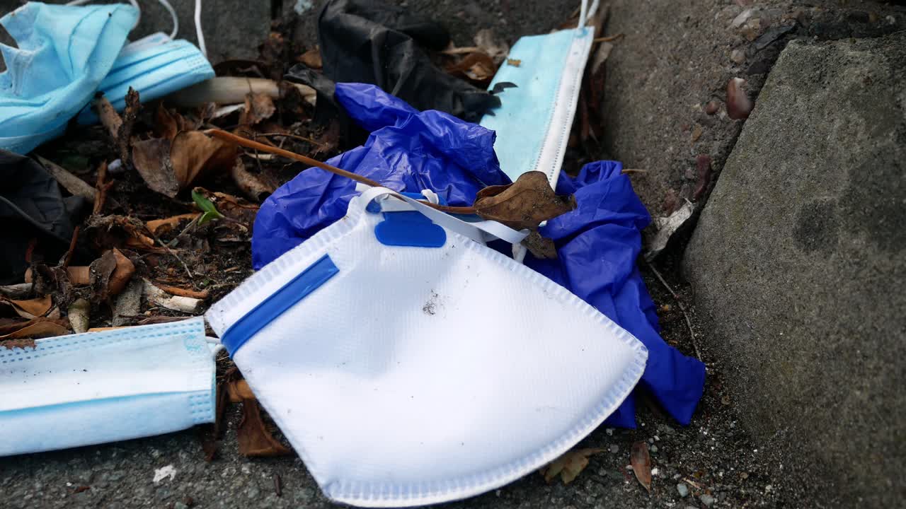 더러운 일회용 코로나 바이러스 안면 마스크와 라텍스 장갑이 거리 연석 하강 돌리 왼쪽에 있는 담배 쓰레기 사이에 있습니다.
