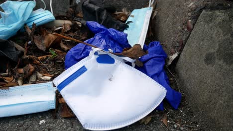máscaras faciales desechables sucias del virus de la corona y guantes de látex entre la basura de cigarrillos en el bordillo de la calle carro descendente a la izquierda