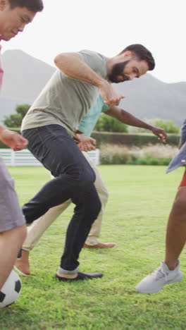 video vertical de amigos varones felices y diversos jugando al fútbol en el jardín