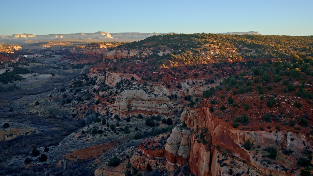 Drone shot at dawn of multicolored high desert canyon with small trees and shrubs