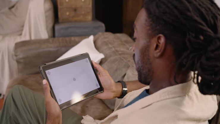 African American man in jacket holding tablet with corner marks aligning tablet on sofa, copy space