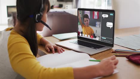 Schoolgirl-using-laptop-for-online-lesson-at-home,-with-boy-raising-hand-and-webchat-on-screen