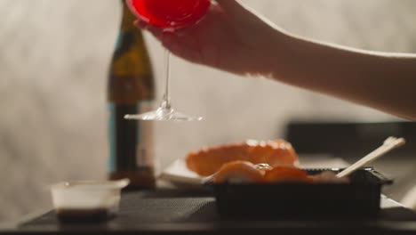 Lady-takes-glass-of-drink-having-dinner-with-sushi-rolls