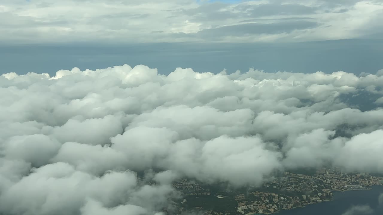 Scenic view from airplane flying through clouds over coastline and city below