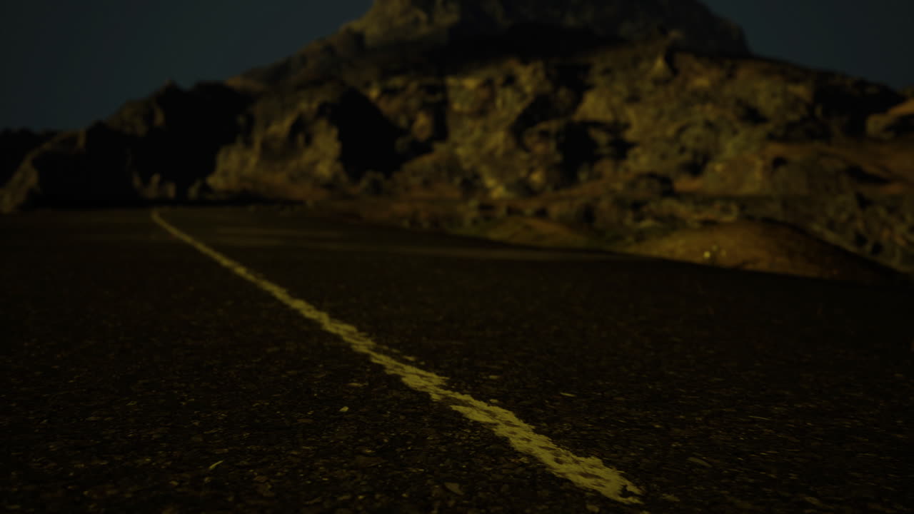Road through rocky terrain under night sky with distant mountain view