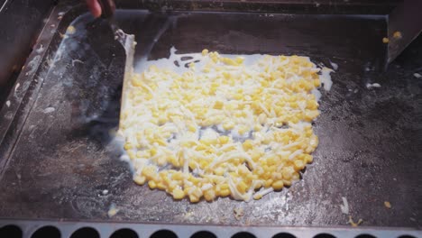a vendor grills taiwanese street food corn topped with melting cheese, creating a deliciously smoky and creamy treat at a bustling night market