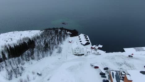 drone view in tromso area flying over finnsnes in winter and showing the sea next to the snowy town with a hotel in norway