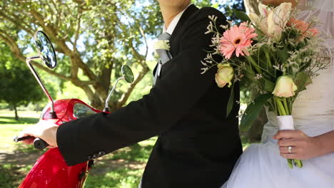 happy newlyweds riding a red scooter in the park