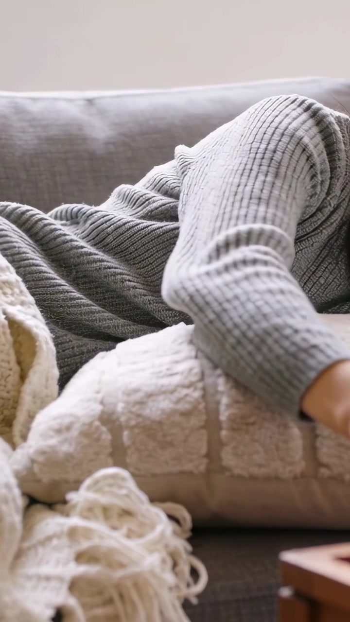 Video verticale: Braccio destro che si muove sul cuscino, adulto con maglione grigio che raggiunge un tavolo di legno sul divano