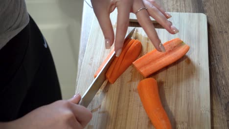 Frau-Schneidet-Karotten-Mit-Einem-Messer-In-Der-Küche-Auf-Einem-Holzschneidebrett