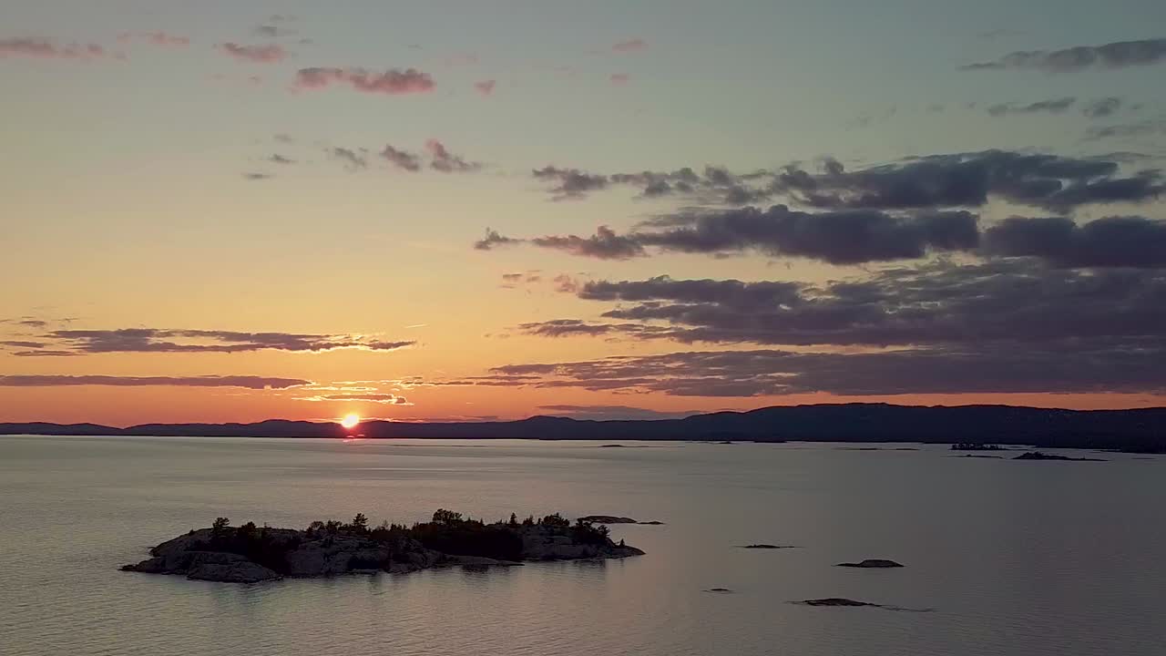 Vista elevada de una isla rocosa con pinos en un lago azul al atardecer, toma aérea amplia de dron con retroceso.