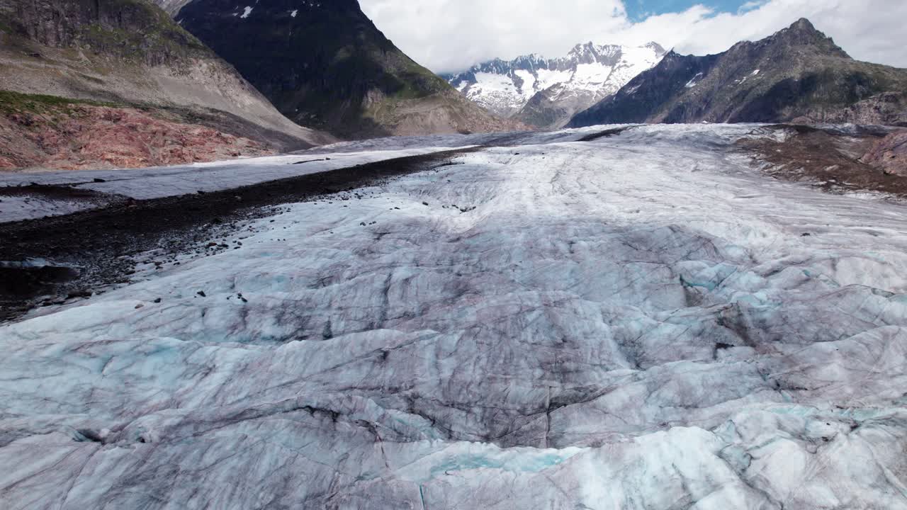 Flugaufnahme einer 4K-Drohne von einem Alpentalgletscher, die Oberflächenablation, Mittelmoränen und Spaltenmuster zeigt und Gletscherdynamik, Erosionsprozesse sowie den fortschreitenden Eisverlust veranschaulicht
