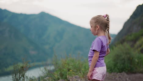 pretty little girl yawns on hill against large mountains