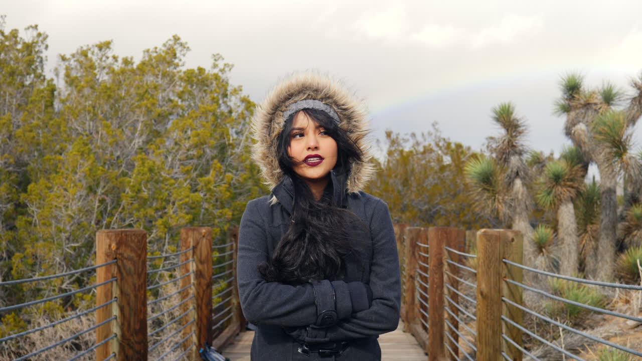 느린 동작으로 비가 내린 후 흐리고 폭풍우가 치는 하늘에 조슈아 나무와 무지개를 들고 사막을 걷는 뜨거운 소녀